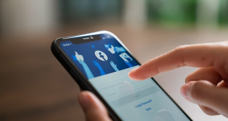 Рука нажимает на экран Facebook на смартфоне