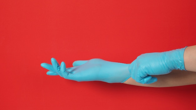 Photo hand is pulling blue latex gloves or surgical gloves on red background.