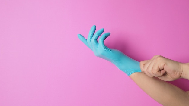 Hand is pulling rubber gloves or blue latex glove on pink background