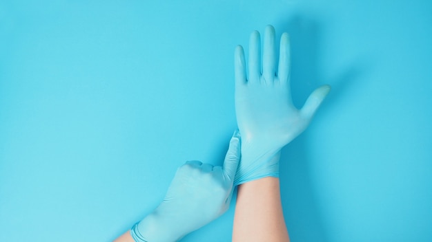 Hand is pulling surgical gloves on blue or Turquoise background.