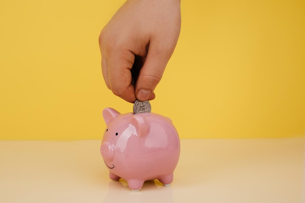 Hand is putting coin into piggy bank saving money concept