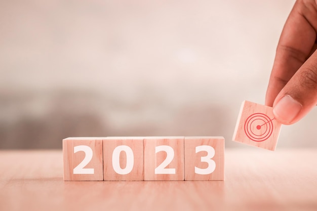 Hand is putting wooden cubes with New year 2023 and goal icon Concept for success in the future goal and passing time Happy new year