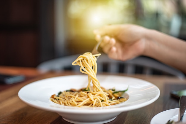 The hand is scooping the spaghetti with a fork