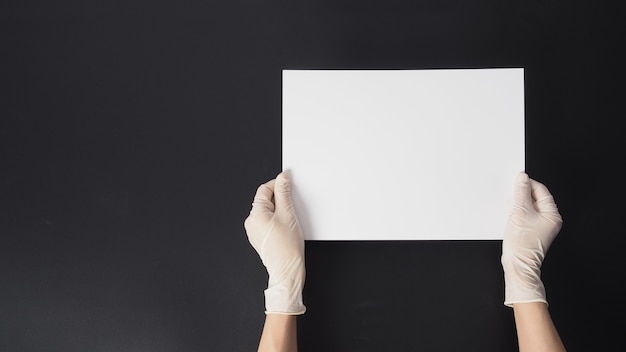 Hand is wear gloves and hold the A4 paper on black background.