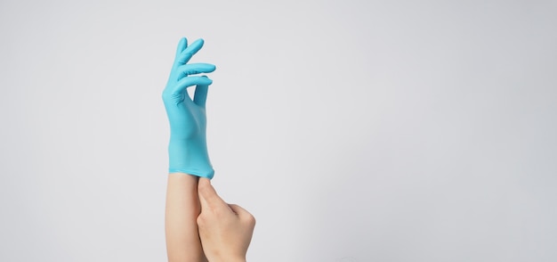 Hand is wearing and pulling blue surgical gloves or latex gloves on a blue background.