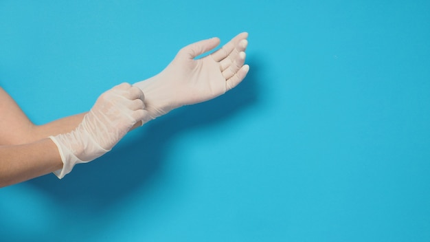 Hand is wearing white medical gloves or latex gloves on blue background.