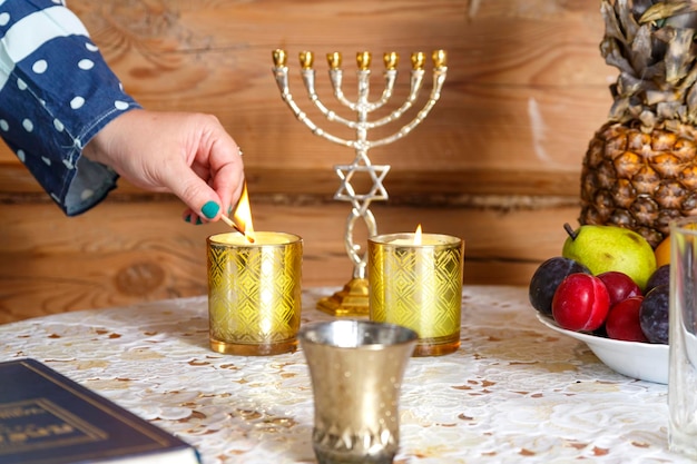 Photo the hand of a jewish religious woman lights shabbat candles at the table