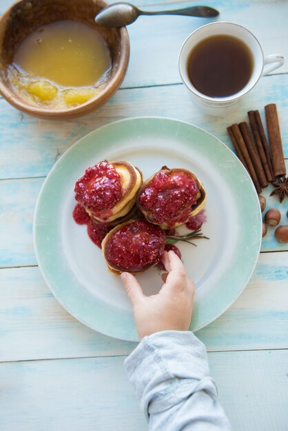 The hand of the kid who takes pancakes with jam