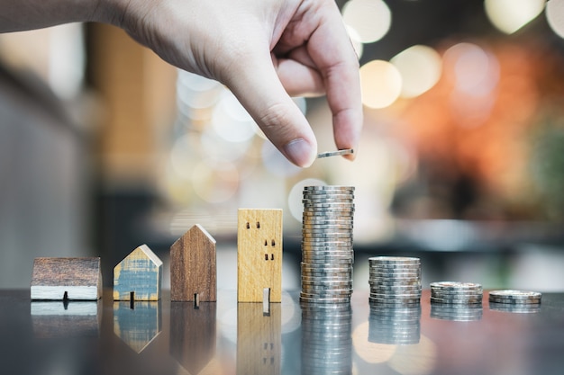 Hand kiezen rij muntgeld op houten tafel en mini houten huis