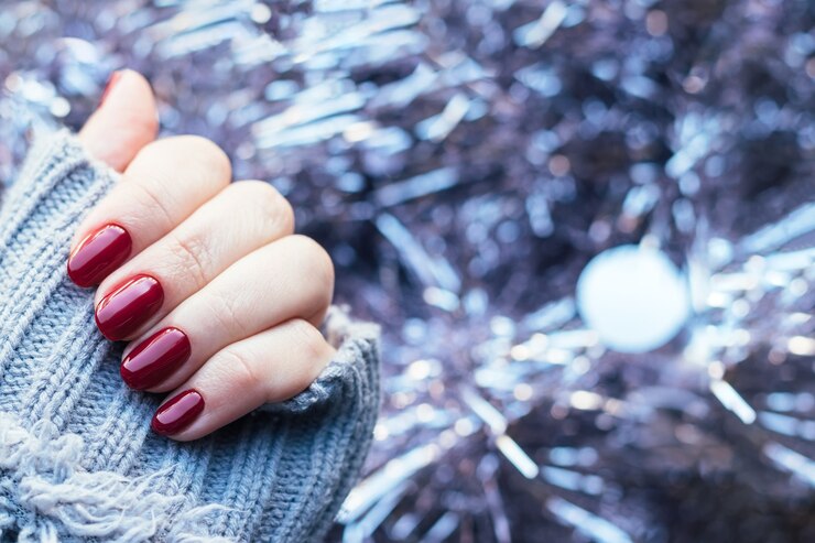 Hand in knitted sweater with burgundy nails on background of pale pink Christmas tinsel garland
