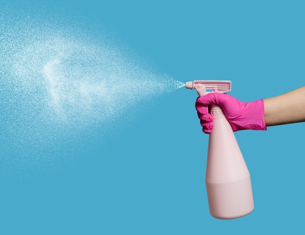 A hand in a latex glove holds a spray bottle on a blue background. Household chores.