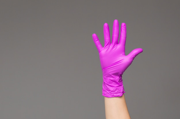 Hand in latex glove with splayed fingers on grey 