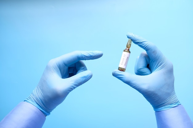 Hand in latex gloves holding glass ampoule vaccine, with copy space