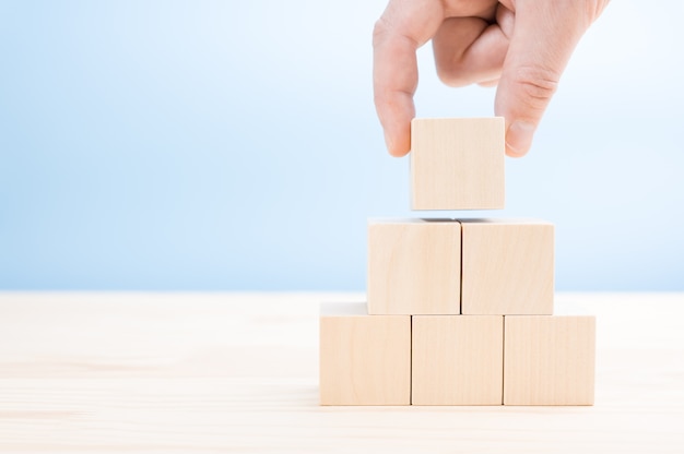 Hand lays out builds a pyramid of blank wooden cubes