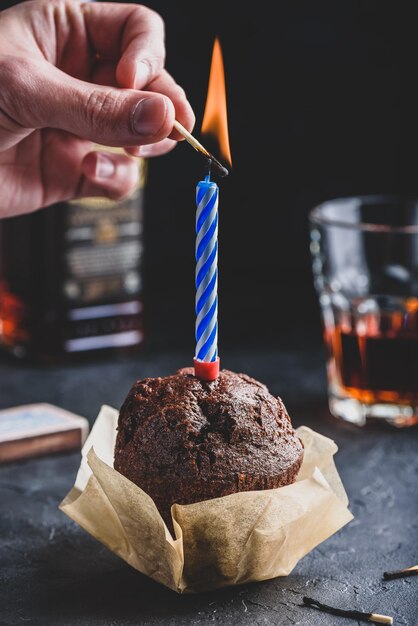 Hand lighting candle with a match on birthday chocolate\
muffin