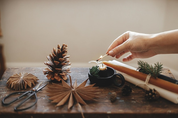 Hand lighting up christmas candle at paper stars pine cones\
scissors rustic scandi hygge advent