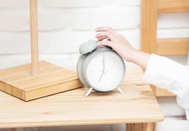 Hand of little asian girl touch alarm clock while she laying on white bed lazy to wake up and put clock stop ringing.