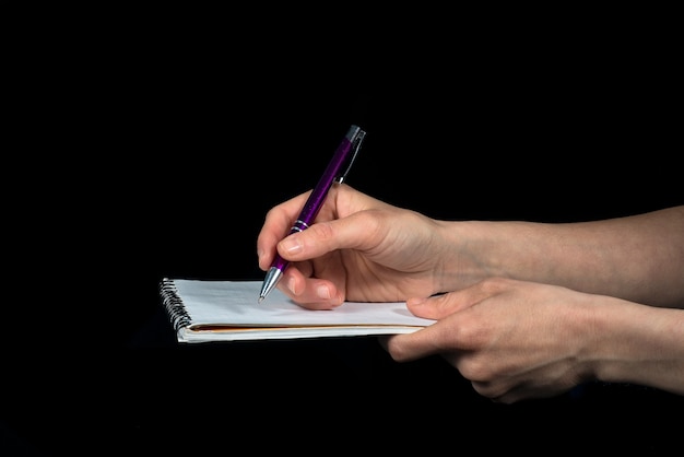 Hand maakt notities op een notitieblok op een zwarte achtergrond