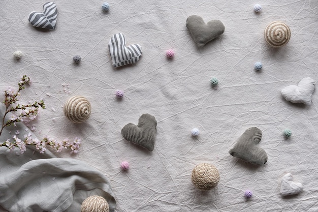 Hand made linen hearts and balls on linen background. Textile handicraft in neutral colors. Springtime flower twigs. Hand hold soft heart. Monochromatic look, desaturated hues. Rustic seasonal decor.