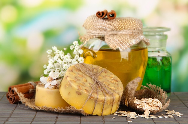 Hand made soap and ingredients for soap making on bamboo mat on green background