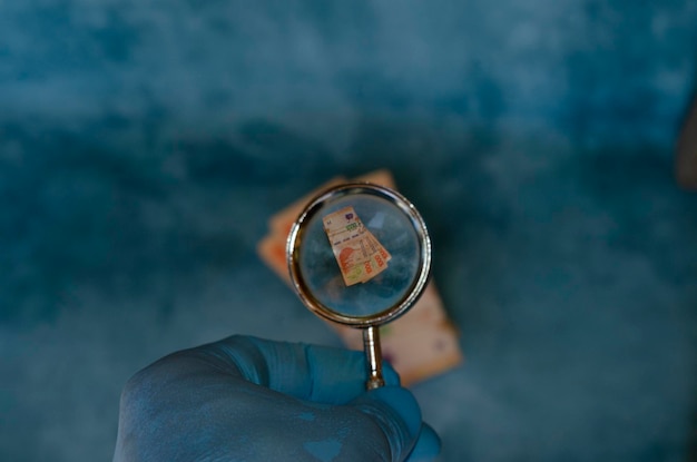 Photo hand magnifying glass on 1000 peso bills marking the devaluation of the argentine currency