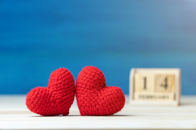 hand make two yarn red heart in front of wooden block calendar