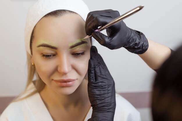 The hand of a makeup artist in black gloves applies a yellow eyebrow paste to the eyebrow Professional stylish permanent makeup eyebrow tinting Close up