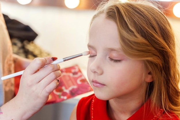 Mano del maestro del trucco che applica l'ombretto per il modello di una bambina carina