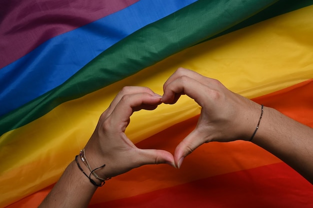 Hand making a heart sign over LGBT rainbow flag