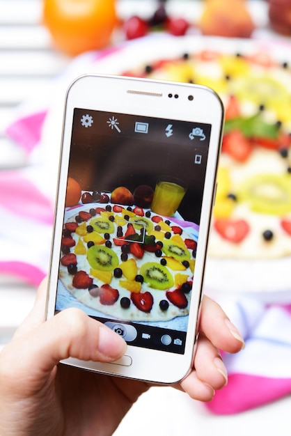写真 ソーシャルネットワーク用に携帯電話でフルーツピザの写真を手作りする