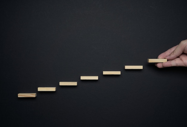 Фото Рука делает деревянную лестницу на черном фоне, карьерный рост и концепции прогресса.