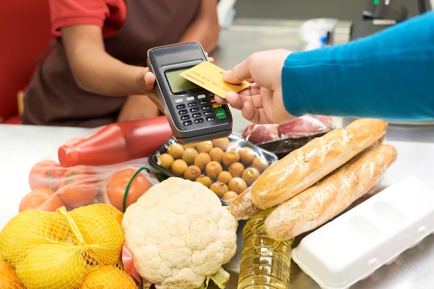 Hand of male consumer holding credit card over screen of payment terminal