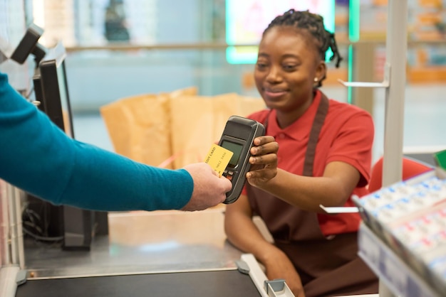 Hand of male customer holding credit card close to screen of payment terminal