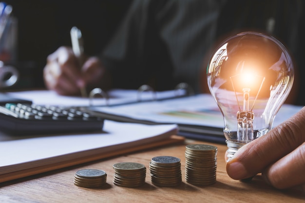 Hand of male holding a light bulb with stack of coins for accounting and creative concept.