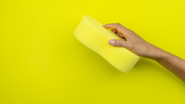 Hand male holding sponge on yellow.