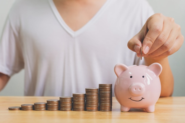 Hand of male putting coins in piggy bank with money stack step growing growth saving money