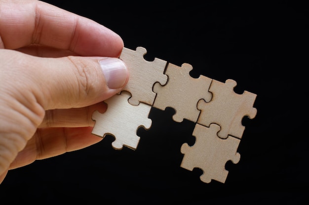 Hand of male trying to connect pieces of jigsaw puzzle