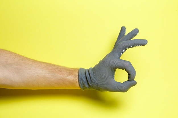 Hand of a man, craftsman, gardener in a gray glove on a yellow background