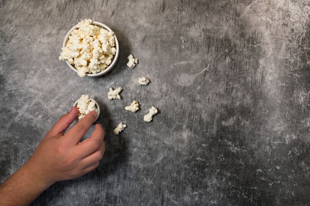 Mano dell'uomo che mangia popcorn, ciotole con popcorn e sfondo grigio. piano del fine settimana o della sera