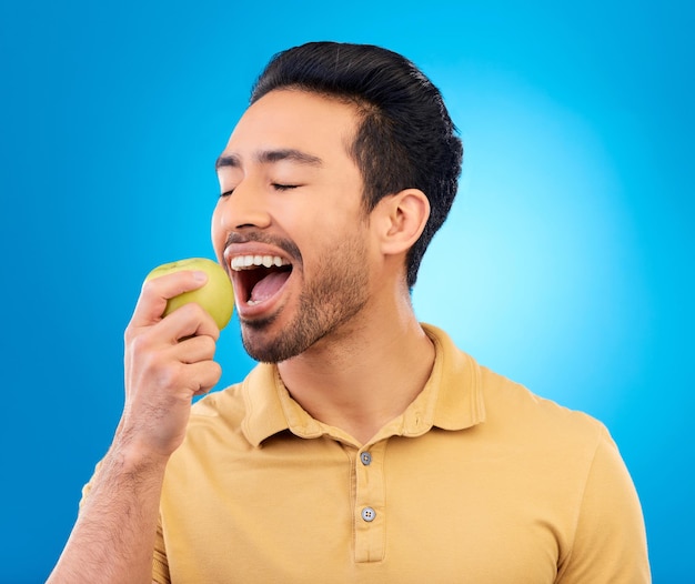 Hand man eet een appel en tegen een blauwe achtergrond voor een gezond dieet Voeding of mockup ruimte geïsoleerd of groen voedsel en mannelijke persoon eet fruit voor gezondheid wellness tegen een studio achtergrond