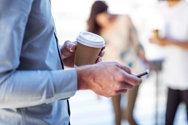 Hand of a man holding cup of coffee, using smartphone