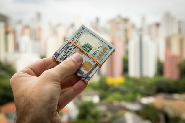 Hand of man holding dollar bills in front of a city landscape