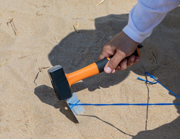 La mano di un uomo che tiene un martello martella in chiodi d'acciaio di alluminio per fissare una tenda da campeggio.