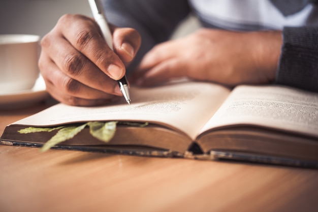 The hand of a man holding a pen and taking notes in a notebook.