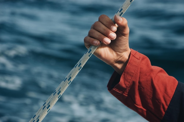 Hand of a man holding on the rope with the waves of the sea in the background