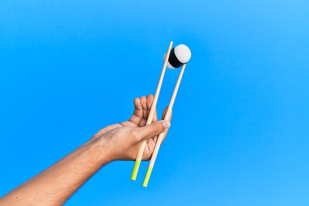 Hand of man holding sushi with chopsticks over isolated blue background