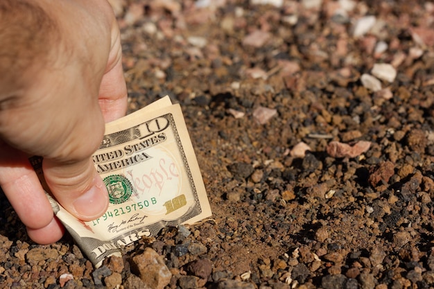 土の地面に折りたたまれた10ドル紙幣を置く男の手不動産投資家土地投資