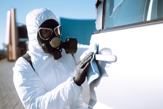 Mano dell'uomo in tuta protettiva per il lavaggio e la disinfezione delle maniglie di un'auto