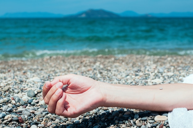 Hand of a man relaxing on a beach, turquoise sea water in the background