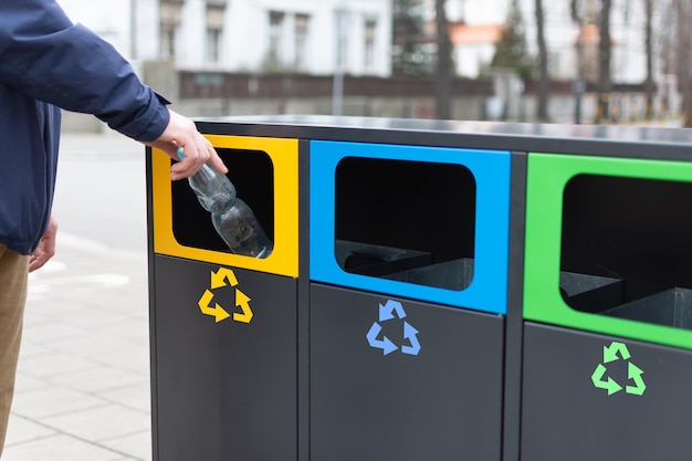 Hand of man throwing plactic bottle into trash bin for plastic waste